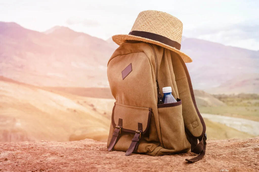 Backpack, water bottle and wide-brimmed sun hat arranged on the ground