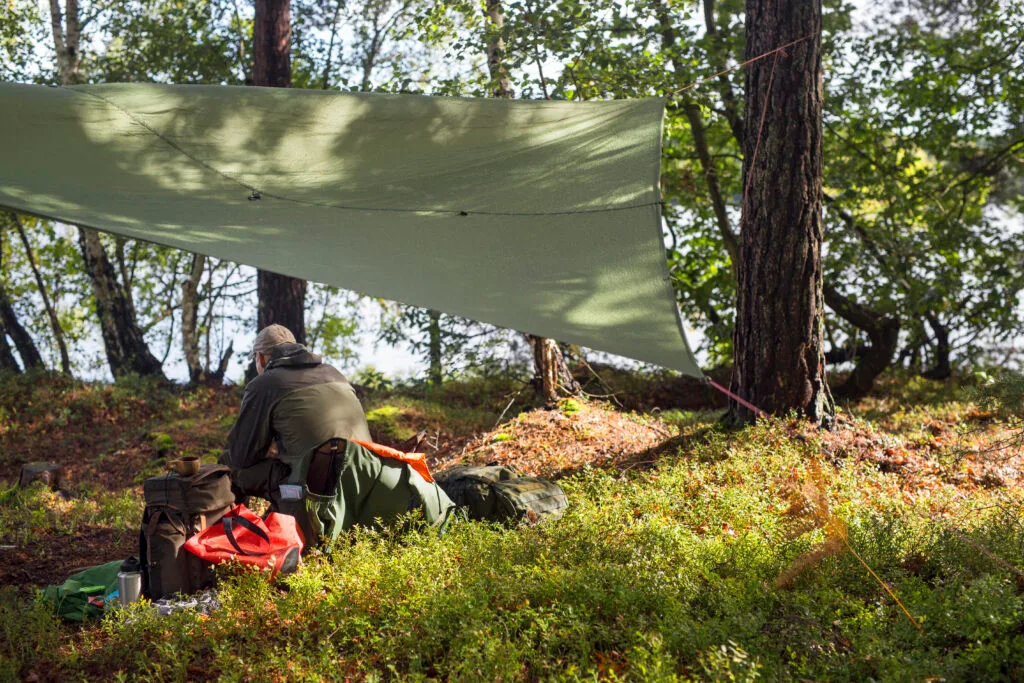 Hiker sheltering under a lightweight tarp shade in the field
