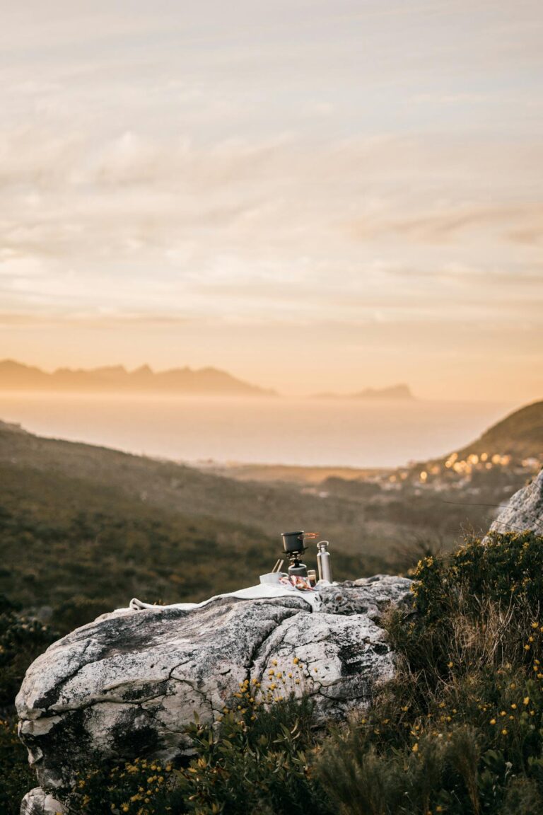 Outdoor cooking setup on a mountain rock at sunrise with breathtaking scenery.