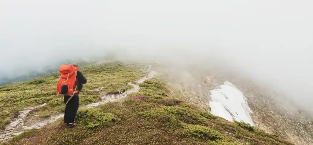 Man hiking with backpack high in the green mountains in spring. Landscape observation during a short break