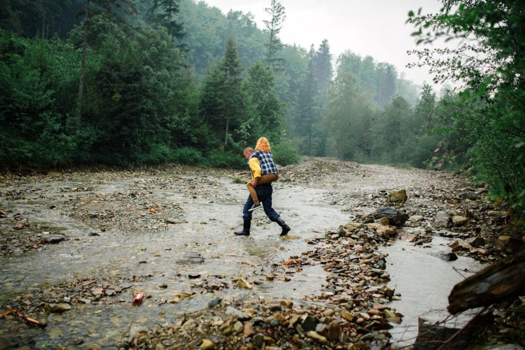rainy day hike, Playful happy handsome couple having while walking in woods. tourists in the mountains. Adventure in nature concept