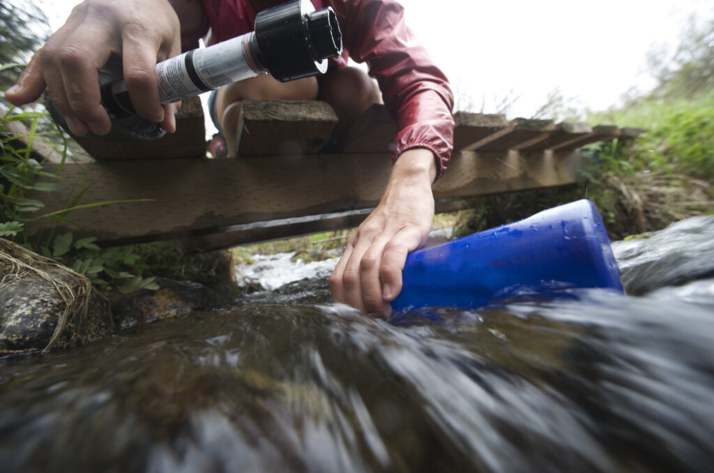 Surface view of female hiker with water filter filling water bottle in stream