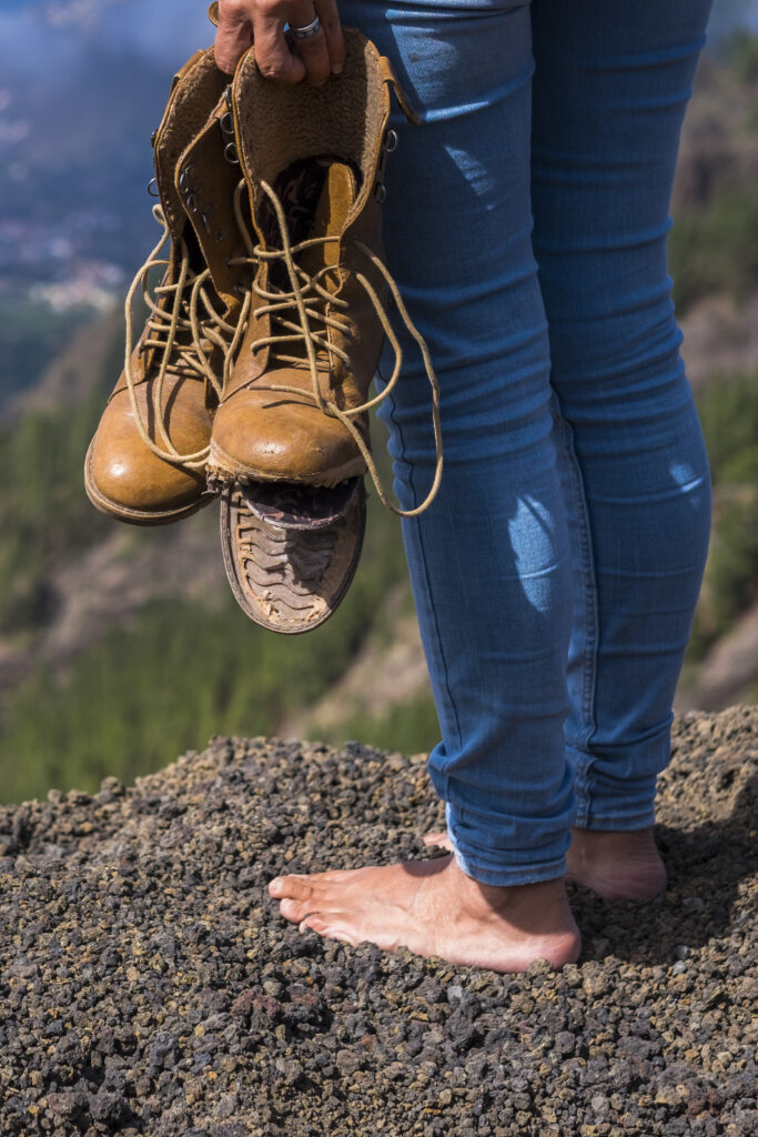 Travel and wanderlust lifestyle concept with barefoot woman stand up with broken shoes on hands looking at the view on the top of the mountain