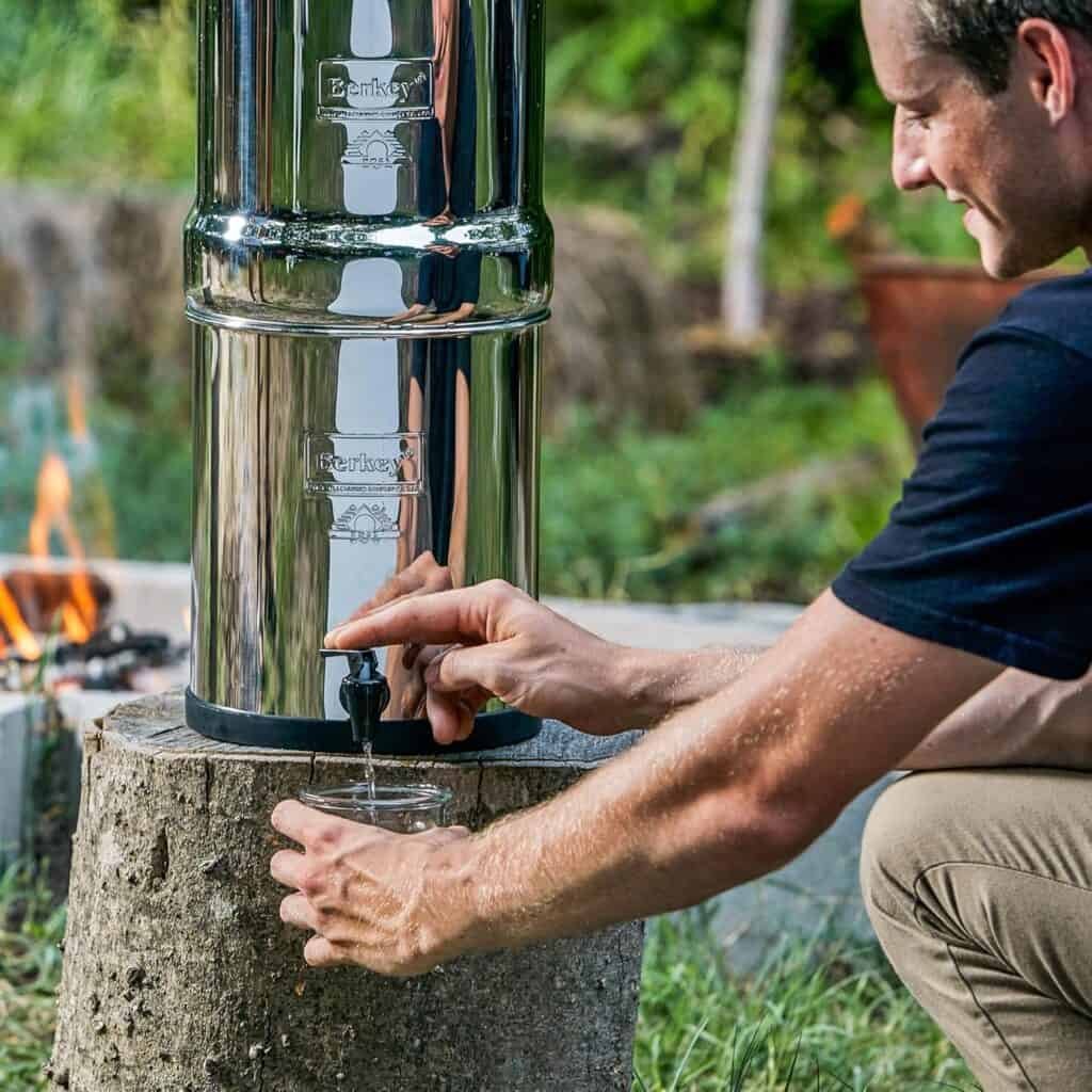 Stainless steel water dispenser outdoors, eco-friendly hydration solution during camping, hiking or outdoor activities, with a person filling a cup from the tap.