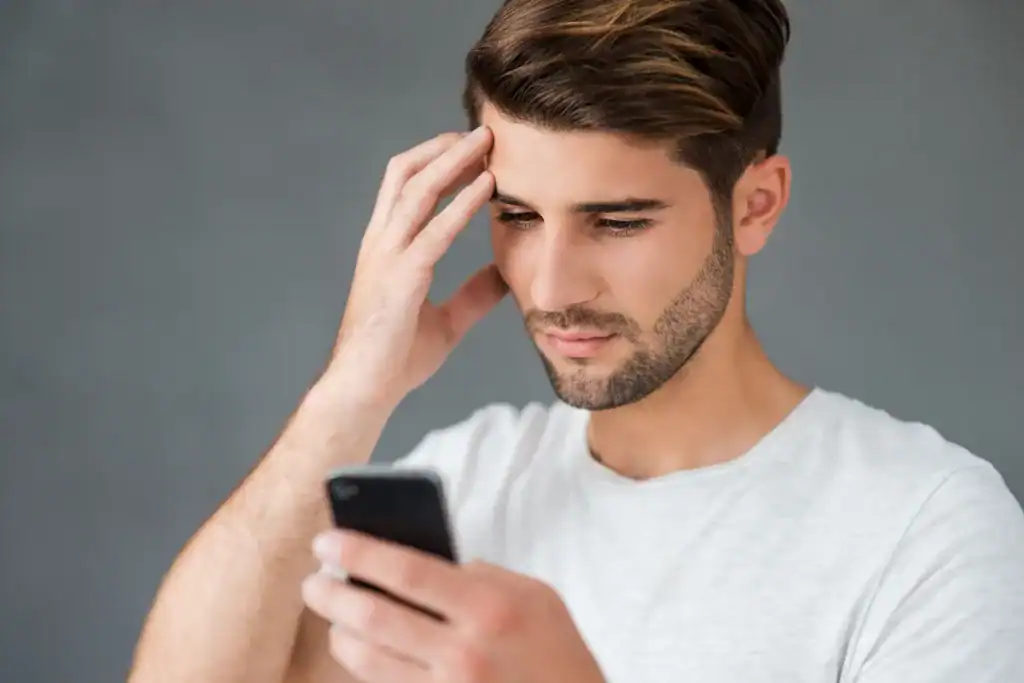 Feeling stressed or anxious, young man holding his head while looking at his smartphone.
