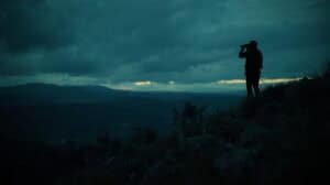 Silhouette of a hiker with binoculars on a mountain at dusk, exploring nature and outdoor adventure, emphasizing wilderness and remote travel experiences.