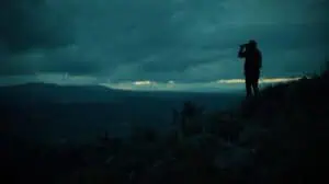 Silhouette of a hiker with binoculars on a mountain at dusk, exploring nature and outdoor adventure, emphasizing wilderness and remote travel experiences.