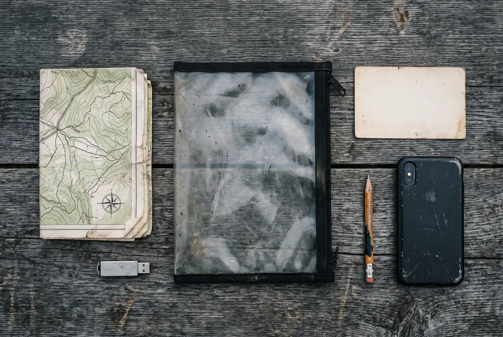 Waterproof document pouch, paper map, encrypted USB drive and index card on weathered barn wood