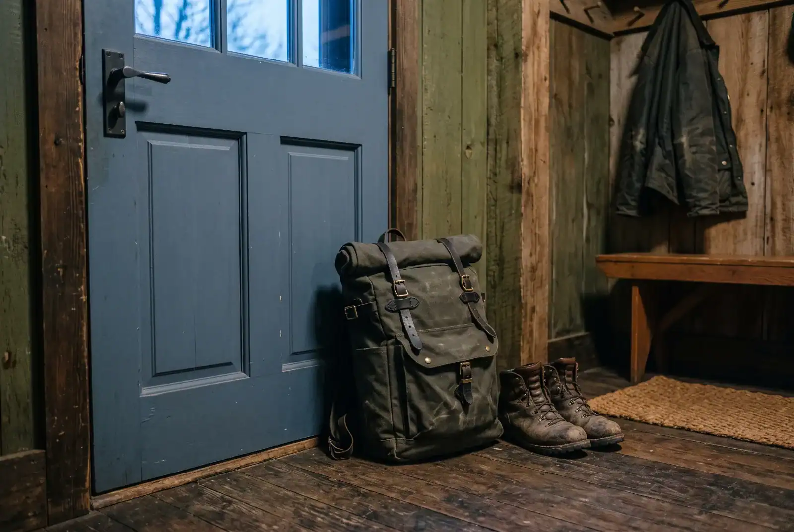 Packed go bag and boots squared away by a door in low evening light