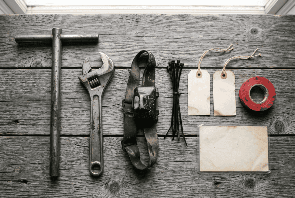 Water meter key, adjustable wrench, headlamp, zip ties and blank tags laid out on barn wood