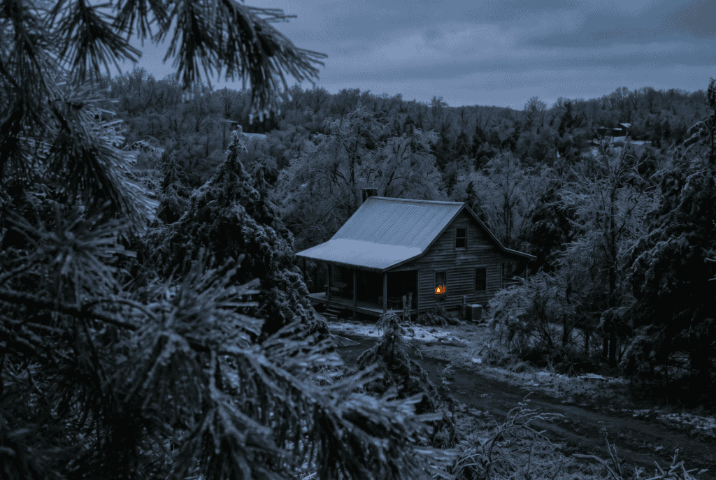 Rural house glazed with ice at blue hour during a power outage, one lantern lit in the kitchen window